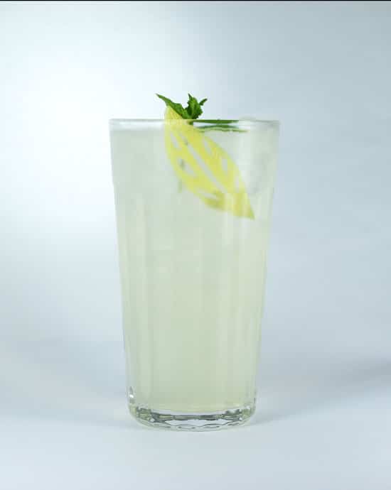 Elderflower sling cocktail in a tall glass with ice and a garnish of mint and carved lemon peel.